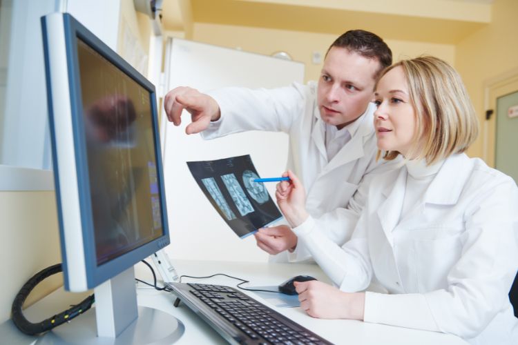 Doctors reviewing MRI images on computer screen and paper.
